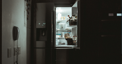 A portable solar generator connected to a kitchen refrigerator during a power outage, featuring solar panels visible through a window and a 24/7 digital overlay.