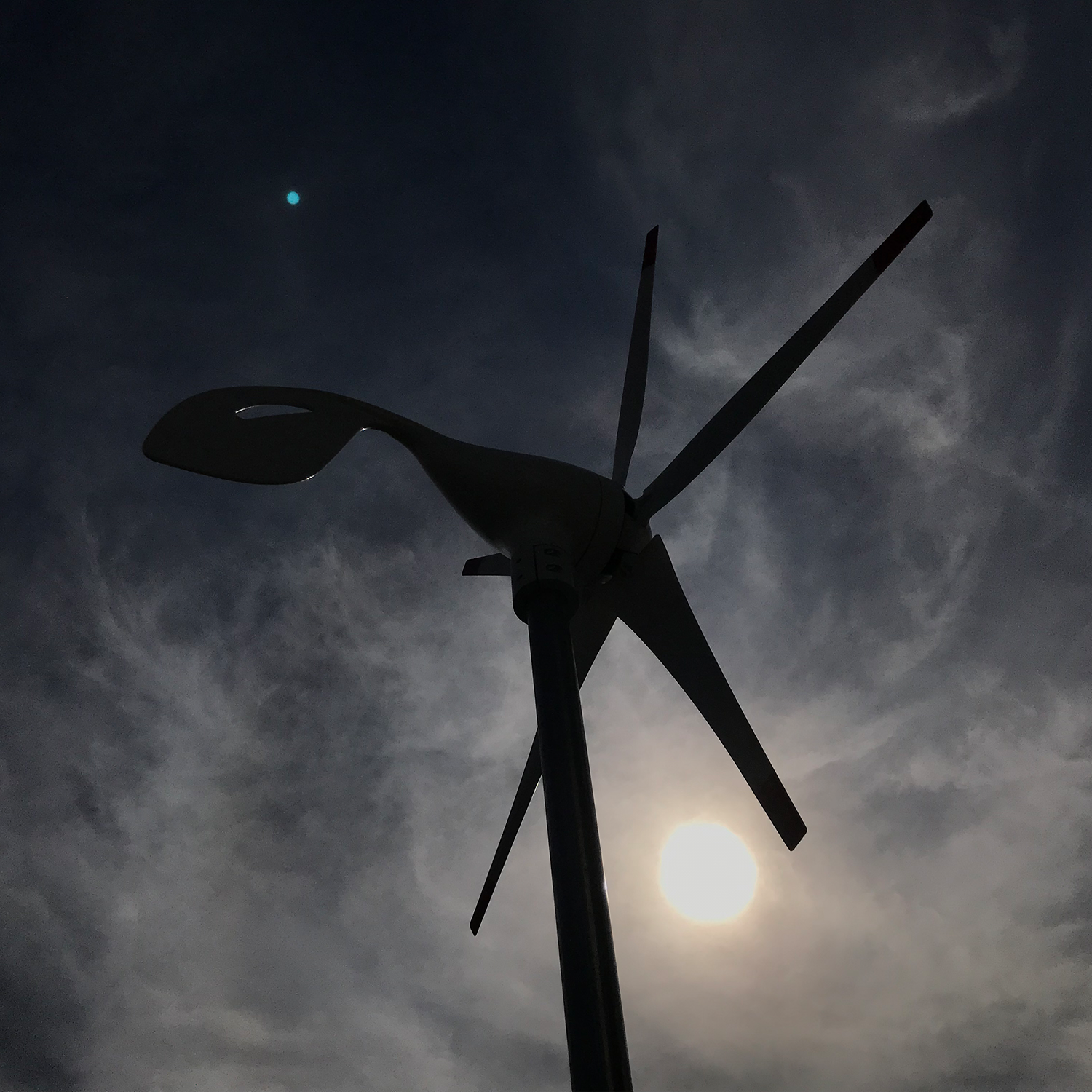 Scene - Silhouette of a wind turbine against a dark sky with clouds and moon.